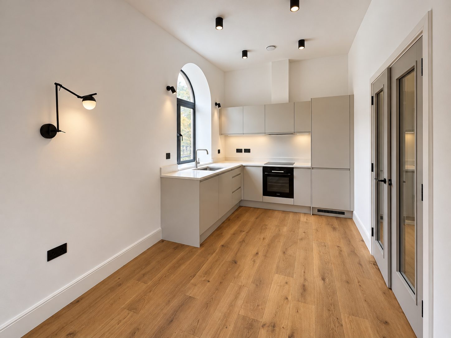Unit 11 kitchen: an arched window above the sink, pale units, black wall lights and wood floors.